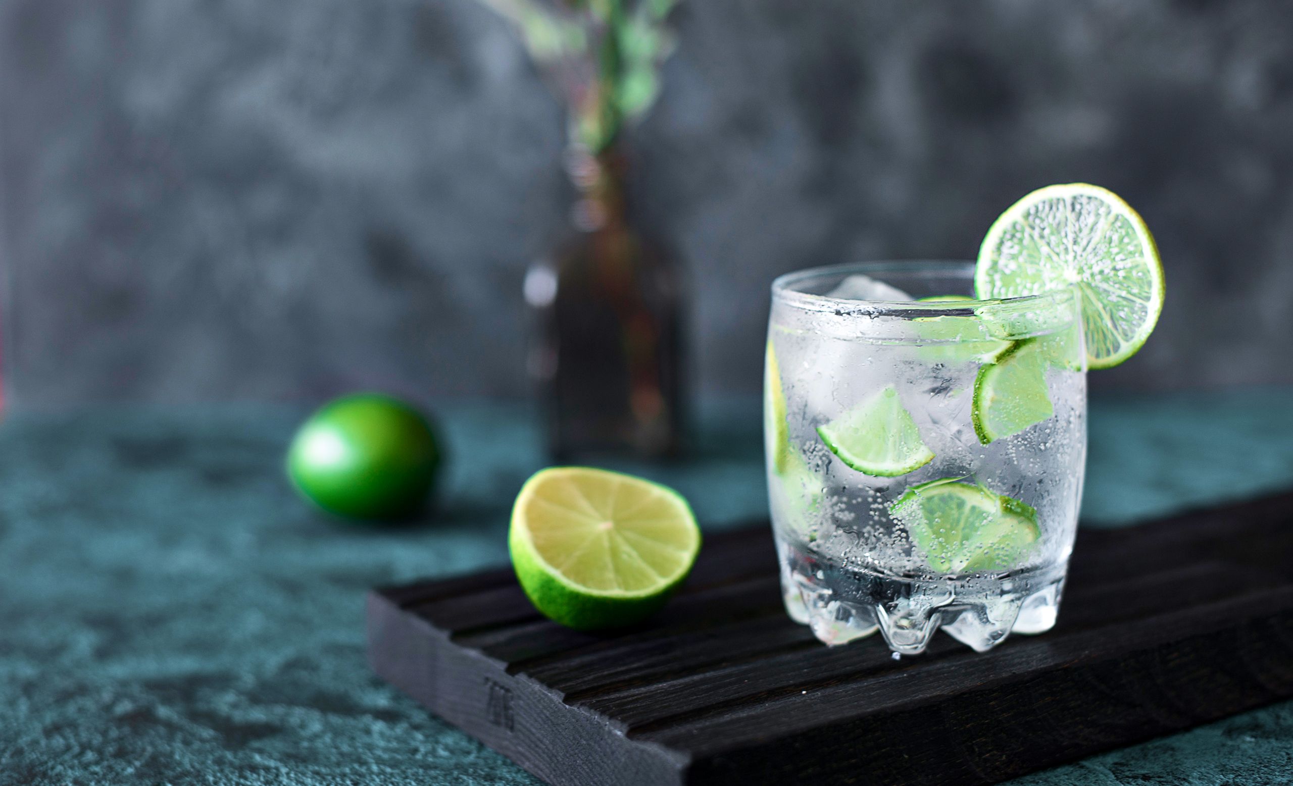Erfrischendes Gin Tonic Glas mit Limettenscheiben und Eiswürfeln auf dunklem Holzbrett
